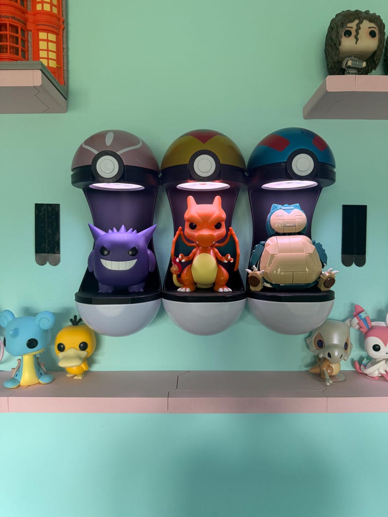 Op de afbeelding: Drie Pok&eacute;mon-thema vitrines, elk met een ander karakterbeeldje. De vitrines zijn gemonteerd op een lichtblauwe muur, met extra beeldjes op een plank eronder. De vitrines zijn ontworpen om op Pok&eacute; Balls te lijken.