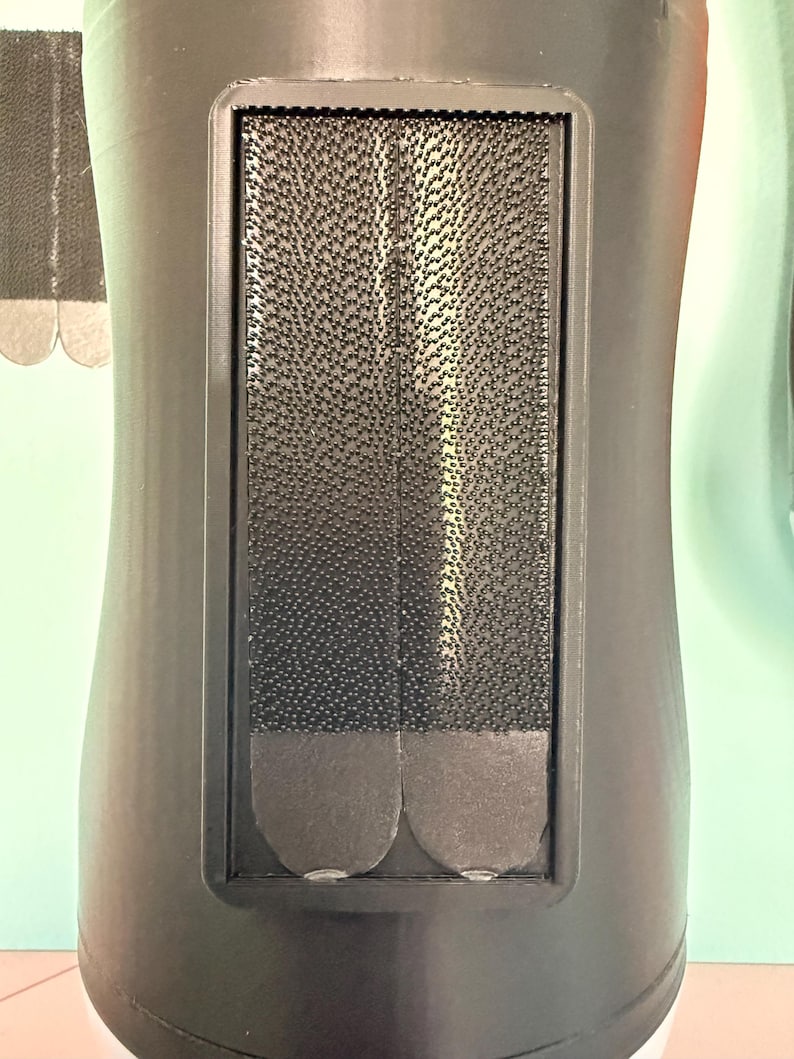 May include: A black plastic mount featuring a rectangular recessed area containing two vertical strips of black hook-and-loop fastener material. The fastener strips have rounded bottom edges and a dense, textured surface for secure attachment.