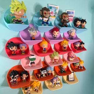 Op de afbeelding: Een verzameling Dragon Ball Z-karakterbeeldjes tentoongesteld op aan de muur gemonteerde, gebogen planken. De planken zijn in verschillende kleuren, waaronder blauw, roze en oranje. De beeldjes tonen personages met stekelig haar en dynamische poses, die het anime-thema benadrukken.