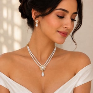 Puede incluir: Un collar de perlas y un juego de pendientes a juego. El collar presenta dos hilos de perlas, un diseño floral central con una perla grande y un colgante de perla en forma de lágrima. Los pendientes tienen un diseño floral similar con una gota de perla.