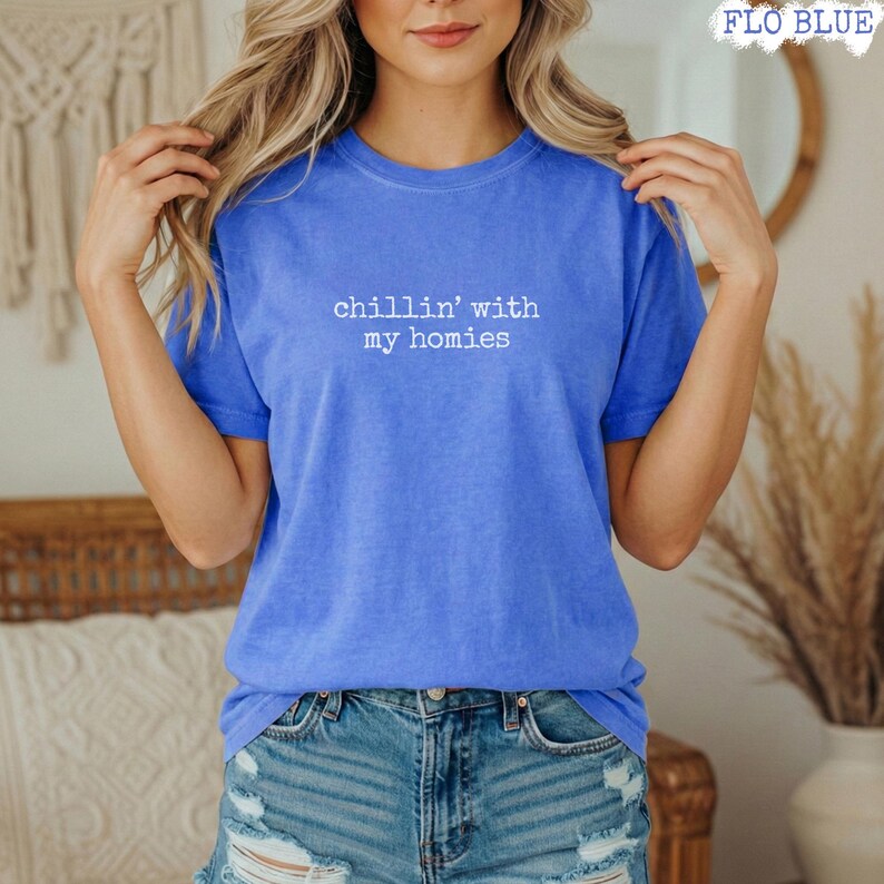 以下が含まれることがあります： 白い文字で「chillin' with my homies」と書かれた青いTシャツ。Tシャツは無地で半袖です。モデルは青いデニムショーツを着用しています。