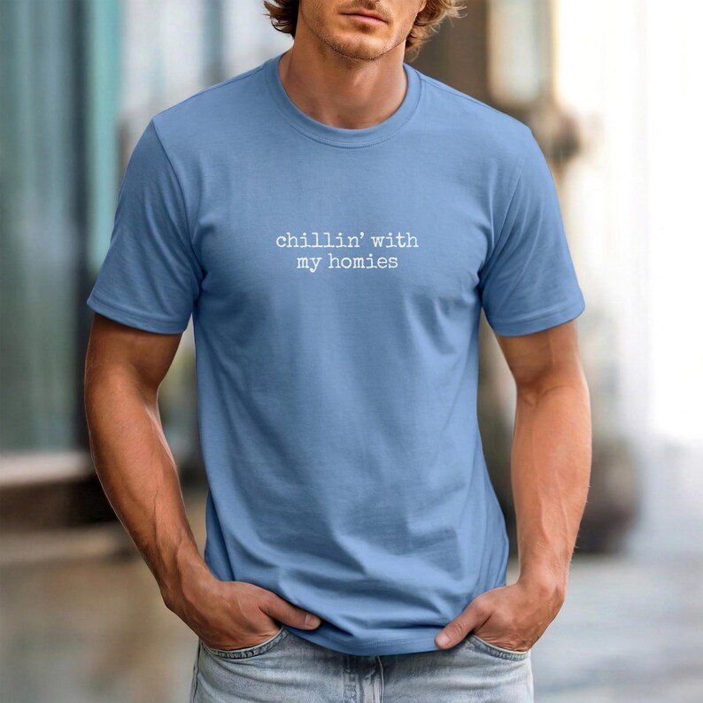 以下が含まれることがあります： 白文字で「chillin' with my homies」とプリントされた水色のTシャツ。半袖とクルーネックのデザインです。柔らかく快適そうな素材で、カジュアルな普段着に最適です。