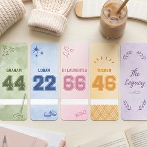Puede incluir: Cinco marcadores personalizados con temática de hockey, con nombres y números. Cada marcador presenta una combinación de colores diferente, incluyendo verde, azul, rosa, naranja y morado. Los marcadores tienen gráficos y texto relacionados con el hockey, como "Graham 44" y "The Legacy".