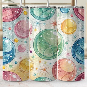 Puede incluir: Tres vasos de acero inoxidable con un diseño colorido y caprichoso. El patrón presenta grandes esferas translúcidas en tonos rosa, azul, verde y amarillo, junto con estrellas y círculos más pequeños sobre un fondo claro.