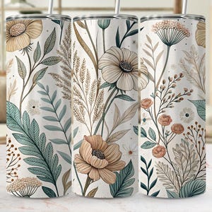 Könnte beinhalten: Drei Edelstahlbecher mit floralen Designs. Die Becher weisen ein sich wiederholendes Muster aus beige, pfirsichfarbenen und teal-farbenen Blumen und Blättern auf weißem Hintergrund auf. Jeder Becher hat einen silbernen Strohhalm.