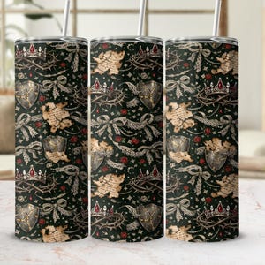 May include: Three stainless steel tumblers with a repeating pattern of crowns, shields, thorns, and scrolls on a dark green background. The design includes red accents and white lace-like bows. Each tumbler has a silver straw.