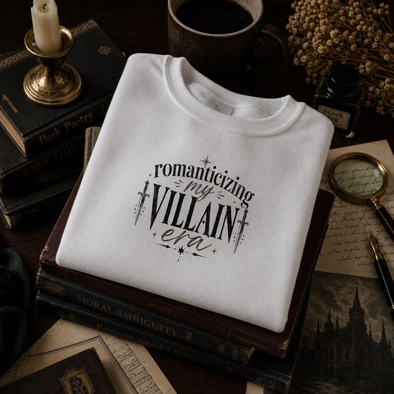 White sweatshirt with "Romanticizing my Villain Era" text and decorative swords.