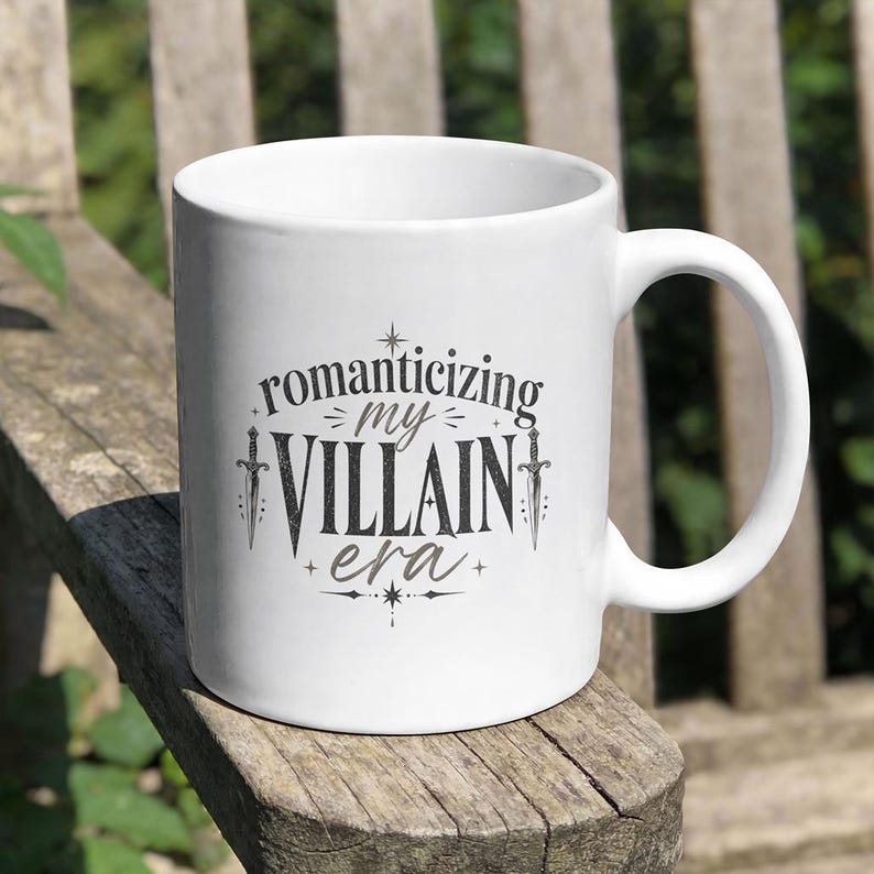White mug with "romanticizing my villain era" text and daggers.