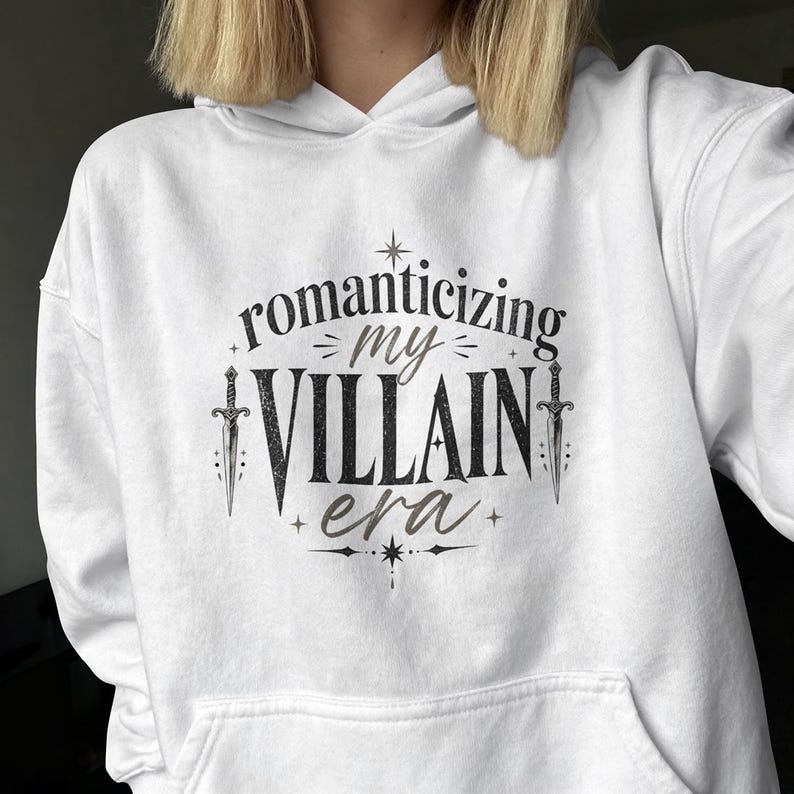 White hoodie with "Romanticizing My Villain Era" text and crossed swords.