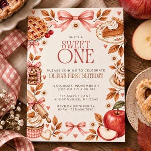 Puede incluir: Una tarjeta de invitación rectangular con fondo crema que presenta ilustraciones en acuarela de pasteles, manzanas, galletas y cintas rosas. El texto dice: SHE'S A SWEET ONE, PLEASE JOIN US TO CELEBRATE OLIVIA'S FIRST BIRTHDAY, SATURDAY, NOVEMBER 7, 2:00 PM TO 4:00 PM, 123 MAPLE LANE, HUDSONVILLE, MI 12345, RSVP BY OCTOBER 24, KARA 123.456.7890.