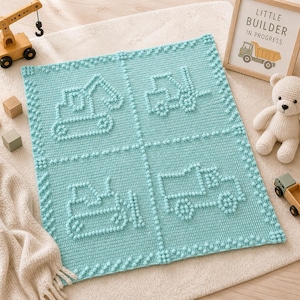 May include: A light blue crocheted baby blanket featuring four squares with construction vehicle designs. The blanket has a textured, dotted pattern and a decorative border. A wooden toy crane, blocks, and a framed sign that says "Little Builder In Progress" are also in the image.