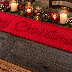 Puede incluir: Un camino de mesa rectangular de color rojo brillante con el texto Merry Christmas en letras texturizadas en relieve. El camino está decorado con patrones de copos de nieve en ambos extremos y tiene un borde tejido en los lados.