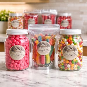 May include: Three glass jars and a clear plastic bag filled with colorful candies. The jars contain pink candies, rainbow-colored candies, and a mix of colorful candies. Each jar has a white lid and a label that says "limekiln".