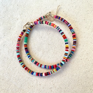 May include: A pair of colorful hoop earrings. The earrings are made of small, flat, round beads in a variety of colors, including red, pink, blue, green, and yellow. The earrings have gold-colored hooks.