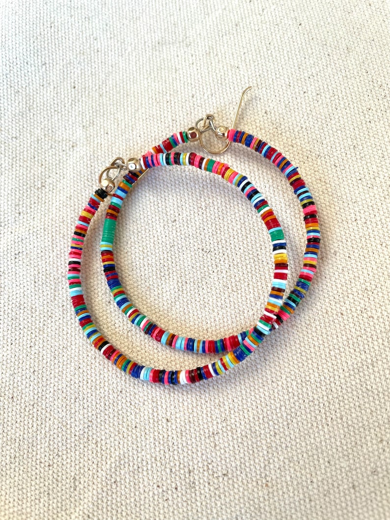 May include: A pair of colorful hoop earrings. The earrings are made of small, flat, round beads in a variety of colors, including red, pink, blue, green, and yellow. The earrings have gold-colored hooks.