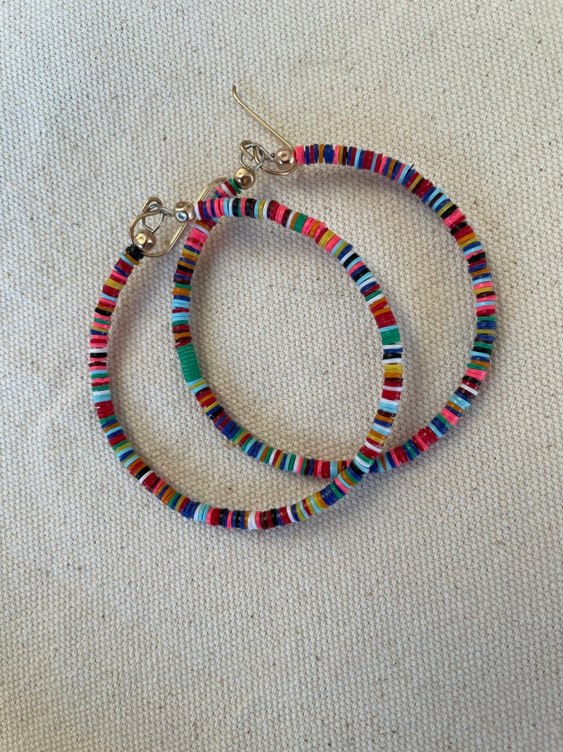 May include: A pair of hoop earrings with a colorful, beaded design. The earrings feature a variety of colors, including red, pink, blue, green, and yellow. The hoops are made of small, flat beads strung together on a wire.