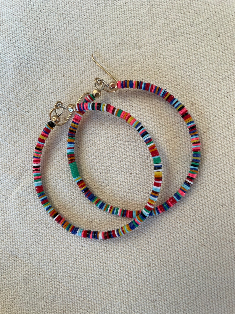 May include: A pair of colorful hoop earrings. The earrings are made of small, flat, round beads in a variety of colors, including pink, red, blue, green, and yellow. The earrings have silver-colored ear wires.