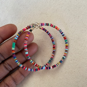 May include: A pair of colorful hoop earrings. The earrings are made of small, flat, round beads in a variety of colors, including red, blue, green, and yellow. The earrings have a gold-colored clasp.