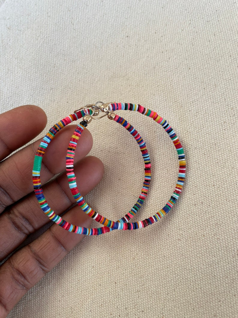 May include: A pair of colorful hoop earrings. The earrings are made of small, flat, round beads in a variety of colors, including red, blue, green, and yellow. The earrings have a gold-colored clasp.