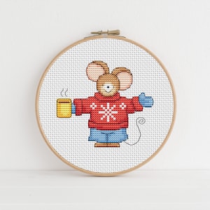 May include: A cross-stitch pattern of a cute mouse wearing a red sweater with a snowflake design, holding a yellow mug and wearing blue mittens. The mouse has a brown nose and a white belly.