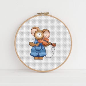 May include: Cross-stitch embroidery of a mouse playing a violin, set in a wooden hoop. The mouse is wearing a blue overall dress and a white shirt. The mouse has tan ears and a tan face. The background is white.