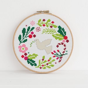 May include: A white dove surrounded by a wreath of green leaves, red berries, and pink flowers. The wreath is decorated with candy canes and snowflakes.