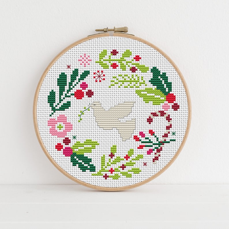 May include: A white dove surrounded by a wreath of green leaves, red berries, and pink flowers. The wreath is decorated with candy canes and snowflakes.