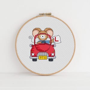 May include: Cross-stitch embroidery in a wooden hoop. The design features a cartoon mouse driving a red car, holding a sign with an "L" on it. The car has a yellow license plate with the text "FT1".