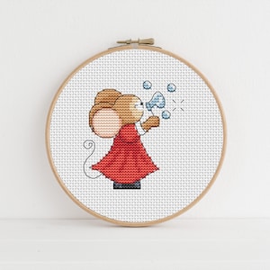 May include: A cross-stitch embroidery hoop with a white background and a cartoon mouse blowing bubbles. The mouse is wearing a red dress and has brown fur.