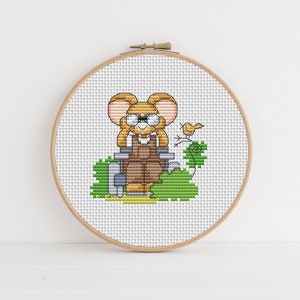 May include: A cross-stitch pattern featuring a cartoon mouse wearing overalls and glasses, holding a pair of gardening shears. The mouse is sitting in a garden with a small bird perched on a branch.