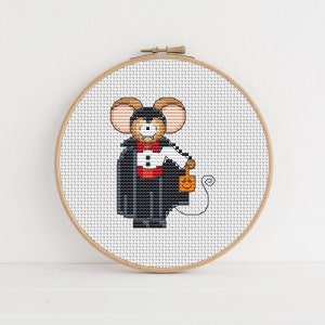May include: A cross-stitch pattern of a cute mouse dressed as a vampire holding a trick-or-treat bag. The mouse is wearing a black cape, a white shirt, and a red bow tie. The bag is orange and has a jack-o'-lantern face on it.