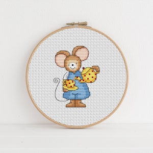 May include: A cross-stitch embroidery hoop with a white background and a brown mouse holding a yellow teacup and a yellow teapot with red accents.