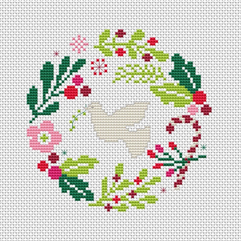 May include: A white cross-stitch pattern of a wreath with green leaves, red berries, and a white dove in the centre.