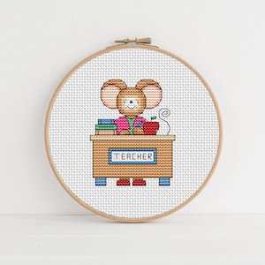 May include: Cross stitch pattern of a mouse teacher sitting at a desk with books, an apple, and a sign that says "Teacher".