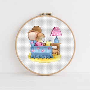 Pode incluir: Um padrão de ponto cruz de um rato castanho sentado em uma poltrona azul lendo um livro com uma lâmpada rosa em uma mesa ao lado.