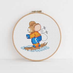 May include: A cross-stitch pattern of a brown mouse wearing an orange and blue ski suit, holding ski poles and skiing on a blue and white background.