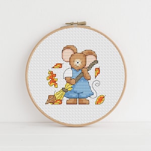 May include: A cross-stitch pattern of a brown mouse wearing blue overalls and holding a broom, surrounded by orange and yellow leaves.
