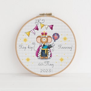 May include: A cross-stitch embroidery hoop with a white background and a cartoon mouse wearing a crown and holding a balloon. The text "Hip hip hooray! 6th May 2023!" is stitched in black thread.