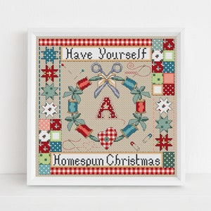 Puede incluir: Patrón de punto de cruz con una corona de artículos de costura con el texto "Have Yourself a Homespun Christmas". La corona está hecha de carretes de hilo, tijeras, botones y agujas. El centro de la corona presenta un corazón rojo y la letra "A".