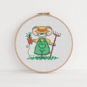 May include: Cross stitch pattern of a cartoon mouse wearing a straw hat, overalls, and glasses, holding a carrot and a rake. The mouse is standing on a green patch of grass.