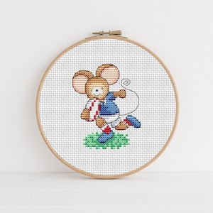 May include: Cross-stitch embroidery of a cartoon mouse playing rugby. The mouse is wearing a blue and white jersey, red and white socks, and blue shoes. It is holding a rugby ball and running on a patch of green grass, set in a wooden embroidery hoop.