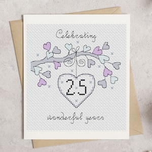 May include: A cross-stitch anniversary card with a brown envelope. The card features a tree branch with heart-shaped leaves in shades of pink and green. The text reads "Celebrating 25 wonderful years" in a handwritten style.