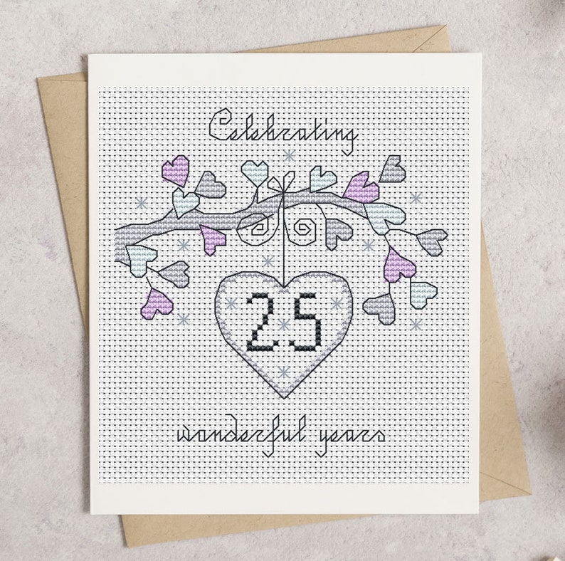 May include: A cross-stitch anniversary card with a brown envelope. The card features a tree branch with heart-shaped leaves in shades of pink and green. The text reads "Celebrating 25 wonderful years" in a handwritten style.