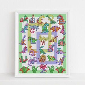 Puede incluir: Un patrón de punto de cruz enmarcado que presenta un alfabeto colorido con cada letra representada por un dinosaurio. Los dinosaurios están en varios colores y poses, con un fondo verde, amarillo y morado.