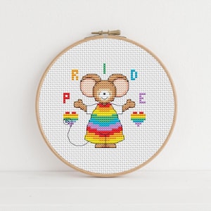 Op de afbeelding: Een kruissteek-borduurring met een witte achtergrond en een cartoonmuis die een regenboogjurk draagt. De letters "PRIDE" zijn rond de muis geborduurd.