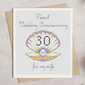 May include: A cross-stitch greeting card with a pearl and shell design. The card reads "Pearl Wedding Anniversary 30 for my wife" in black script. The shell is purple, yellow, and white, with a pearl in the center. The card is on a white background.