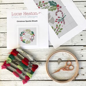 May include: A cross stitch kit featuring a Christmas Sparkle Wreath design by Lucie Heaton Cross Stitch Designs. The kit includes a printed pattern, embroidery floss in various colours, and a wooden embroidery hoop.