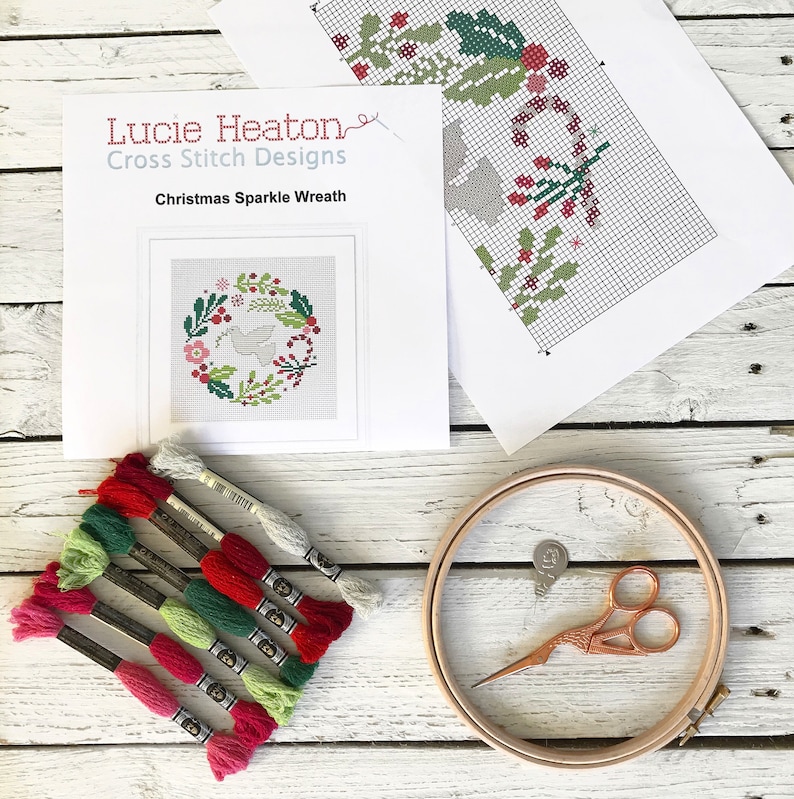 May include: A cross stitch kit featuring a Christmas Sparkle Wreath design by Lucie Heaton Cross Stitch Designs. The kit includes a printed pattern, embroidery floss in various colours, and a wooden embroidery hoop.