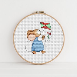Op de afbeelding: Een kruissteek borduurring met een witte achtergrond en een bruine muis die een rode, groene en witte vlieger vasthoudt.