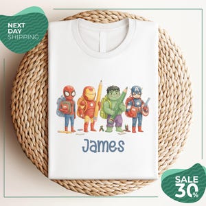 A white t-shirt with a printed design of four superhero characters, including Spider-Man, Iron Man, Captain America, and James, standing together.